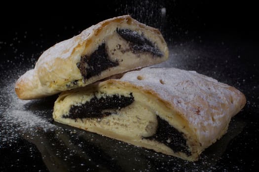 Strudel with poppy seeds sprinkled with powdered sugar cut close-up on a black background