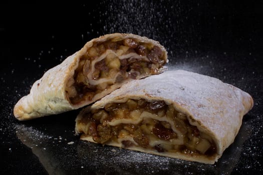 Apple strudel sprinkled with powdered sugar cut close-up on a black background