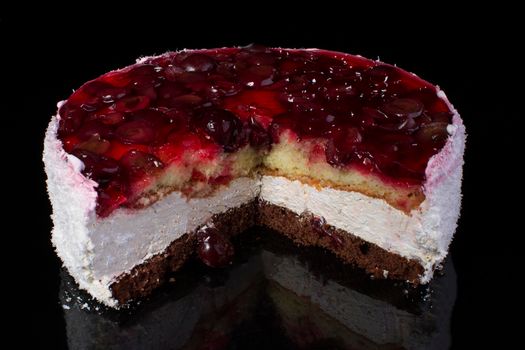 Piece of a large cake in coconut shavings with a cherry in jelly on a black background