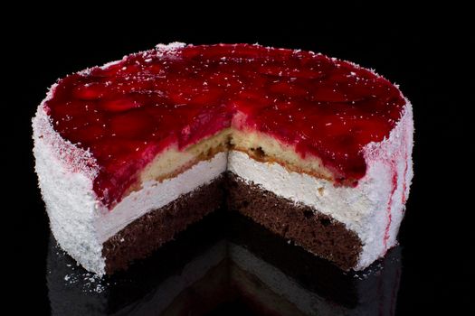 Piece of a large cake in coconut shavings with strawberries in jelly on a black background