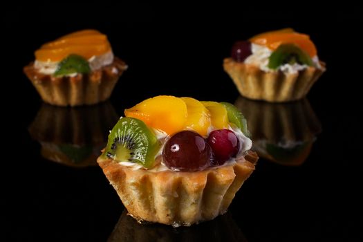 cake basket with kiwi fruit peach gooseberries close-up on a black background
