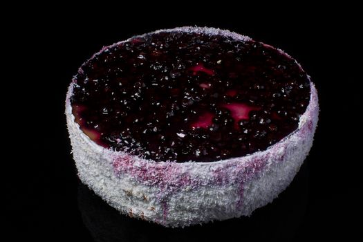 Cake with coconut shavings and currant in jelly on a black background