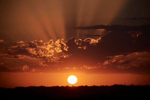 Sunset sun setting behind the horizon, sun rays, orange, clouds