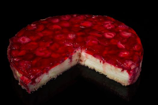cut piece of cake cheesecake with strawberries in jelly on black background