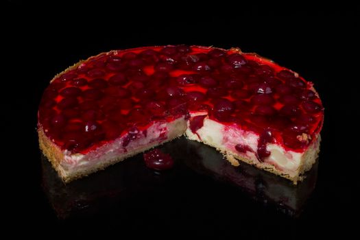 Piece of cake cheesecake with cherry in jelly on black background