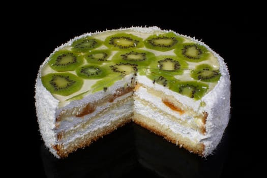 Cut off piece of white festive cake with kiwi and coconut shavings on a black background