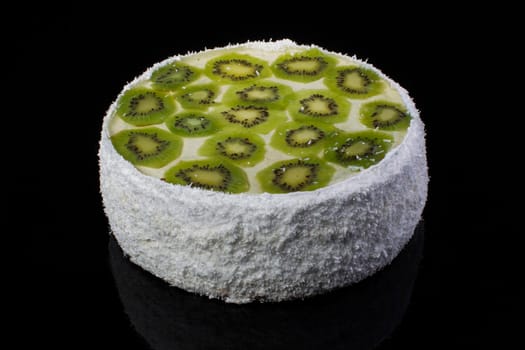 White festive cake with kiwi and coconut shaving on a black background