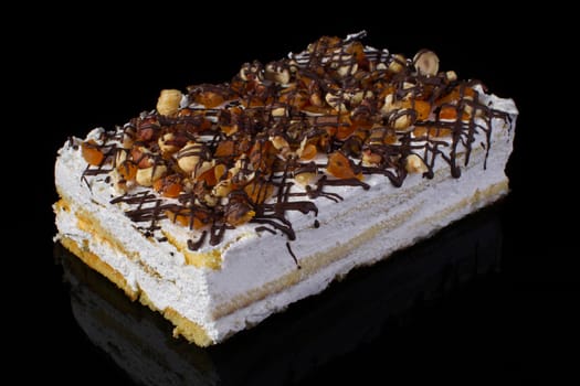 A piece of a cake close-up with a white cream sprinkled with nuts raisins and chocolate