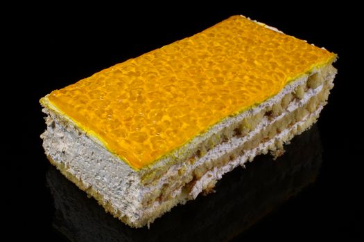 A piece of cake topped with a large plan covered with a yellow glaze made of jelly on a dark background