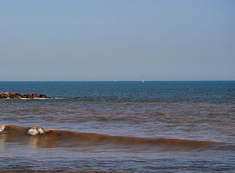 Beach shore with breakwater fishing rods and sailboats, bright day, calm waters