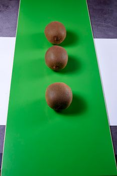 Three kiwis on green background, wood, white background and stone, front view