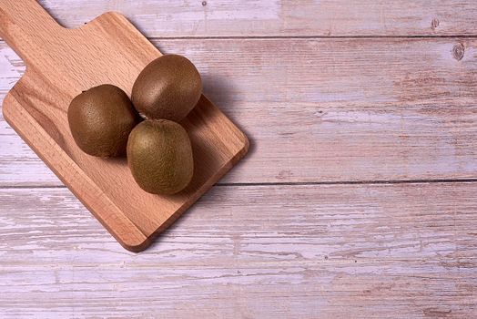 Three kiwis on a wooden board. Wooden floor, empty space, front view.