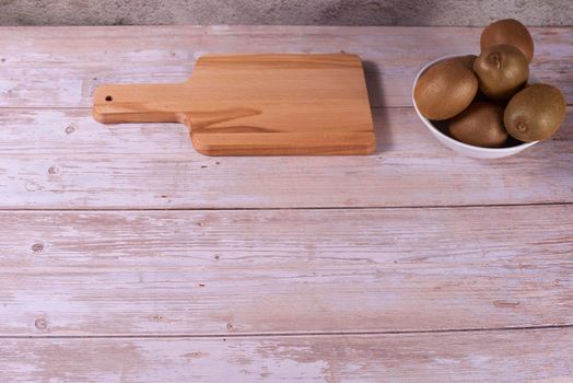 Various kiwis in white bowl and wooden board. Wooden boards, empty space, frontal view, warm tones