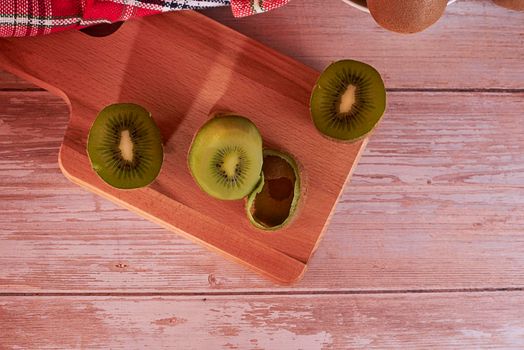 Cut kiwis on wooden board. wooden floor, zenithal view, red and white cloth, empty space.