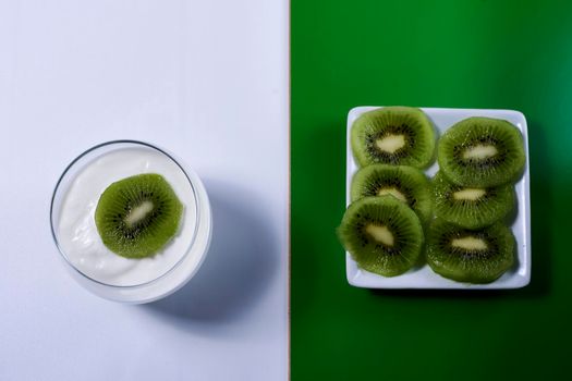 Yoghurt glass with kiwi fruit and plate with kiwi fruit cut on green and white background, rectangles, horizontal, symmetry