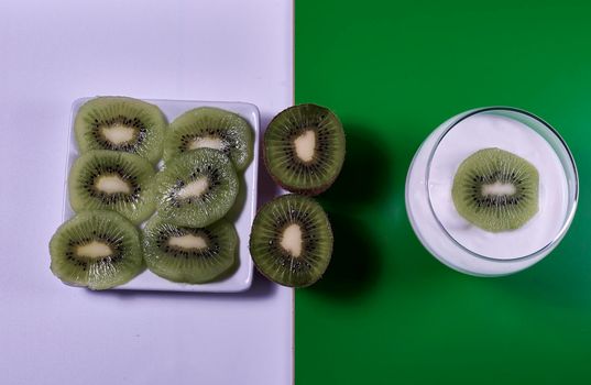 Yoghurt glass with kiwi fruit and plate with kiwi fruit cut on green and white background, rectangles, horizontal, symmetry