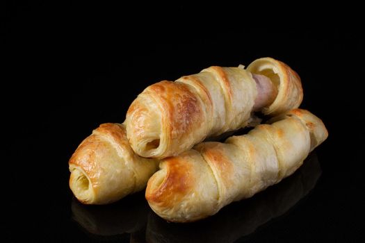Bun with puff pastry with sausage on a dark background