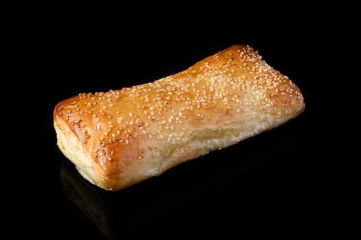 Puff pastry roll with sesame seeds on a black background