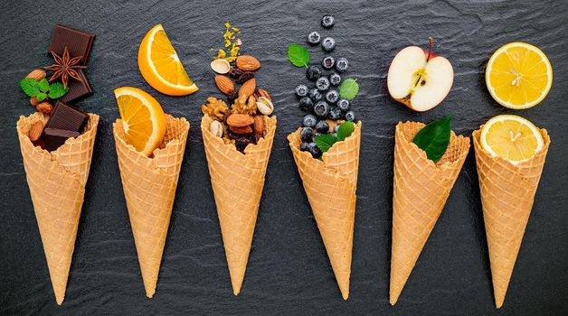 Various of ingredient for ice cream flavor in cones blueberry ,lime ,pistachio ,almond ,orange ,chocolate ,vanilla and coffee set up on dark stone background . Summer and Sweet menu concept.