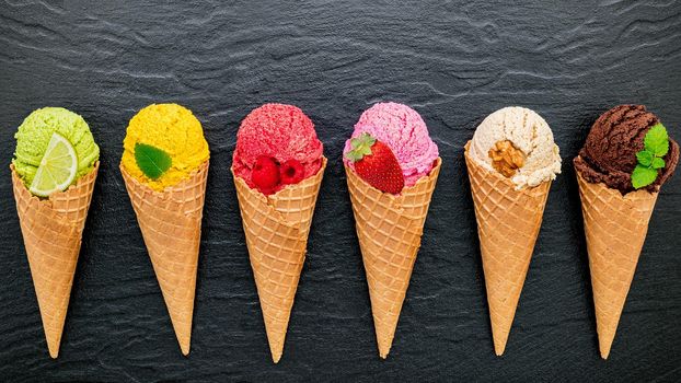 Various of ice cream flavor in cones blueberry ,lime ,pistachio ,almond ,orange ,chocolate ,vanilla and coffee set up on dark stone background . Summer and Sweet menu concept.