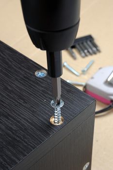 worker screws in a wooden furniture with a screwdriver