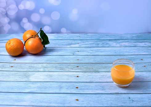 Glass of orange juice on wooden floor with several orange trees and bright background, empty space