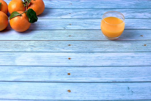 Glass of orange juice on wooden floor with several orange trees and bright background, empty space