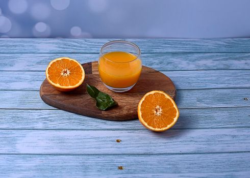 Glass of orange juice on wooden table on wooden floor with nails, halved oranges green leaves