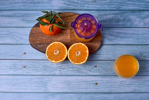 Glass of orange juice, juice squeezer with sliced oranges on wooden table on wooden floor, overhead view