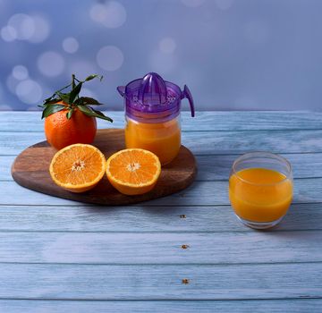 Glass of orange juice, juice squeezer with sliced oranges on wooden table on wooden floor,