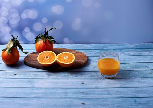 Orange juice glass, juice squeezer with sliced oranges on wooden table on wooden floor, bright background