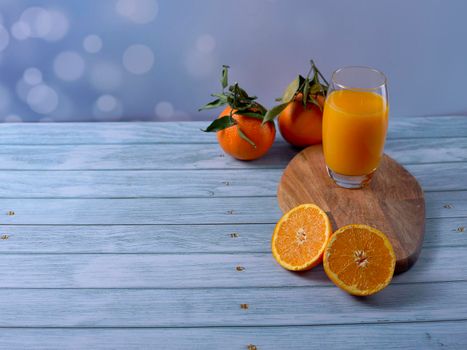 Large glass of orange juice on wooden table on wooden floor with cut oranges and whole oranges and bright background