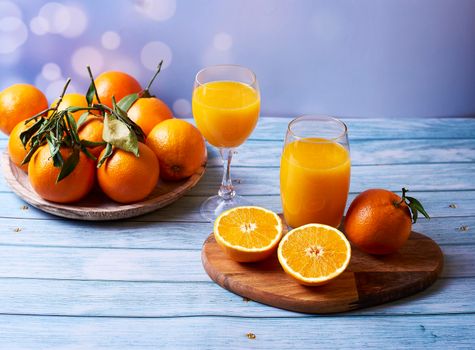 Cup and big glass of orange juice on wooden table with oranges on wooden plate on wooden background