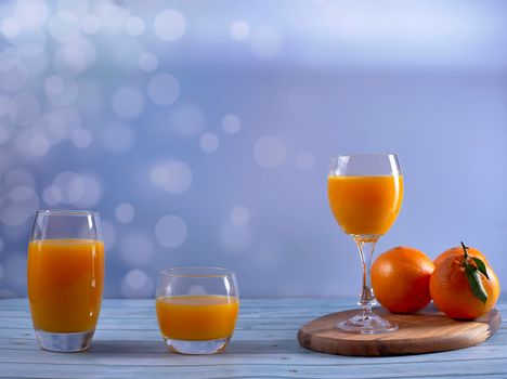 Glass, cup, big glass of orange juice on wooden table and oranges on wooden floor and bright background, front view