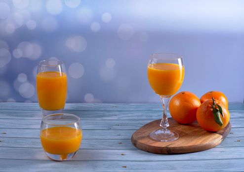 Glass, cup, big glass of orange juice on wooden table and oranges on wooden floor and bright background, front view