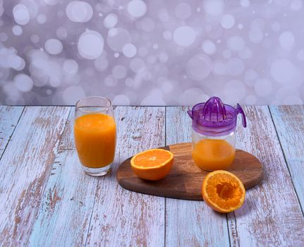 Large glass of orange juice, glass juicer, cut oranges, wooden board and wooden floor