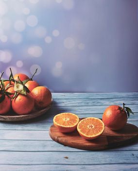Whole oranges on wooden plate, half orange on wooden table, bright background and wooden floor