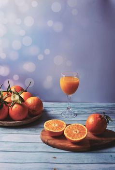 Glass of orange juice with whole and half oranges, on wooden table wooden plate background bright wooden floor