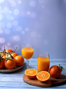 Glass of orange juice with whole and half oranges, on wooden table wooden plate background bright wooden floor