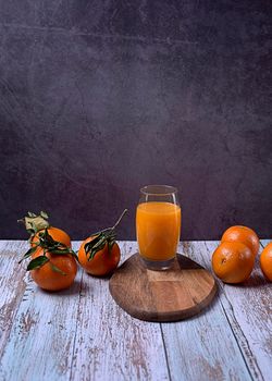 Large glass of orange juice on wooden table with several oranges marble background wooden floor