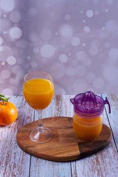 Glass of orange juice. glass juicer, wooden table whole oranges with green leaves bright background