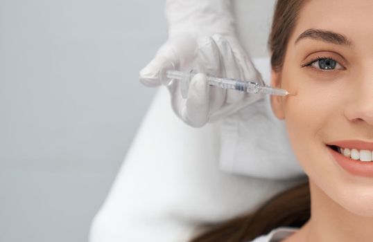 Close up portrait of smiling brunette beautiful woman on procedure injection anti-aging skin in beautician. Concept of process injection for improve the condition face. 