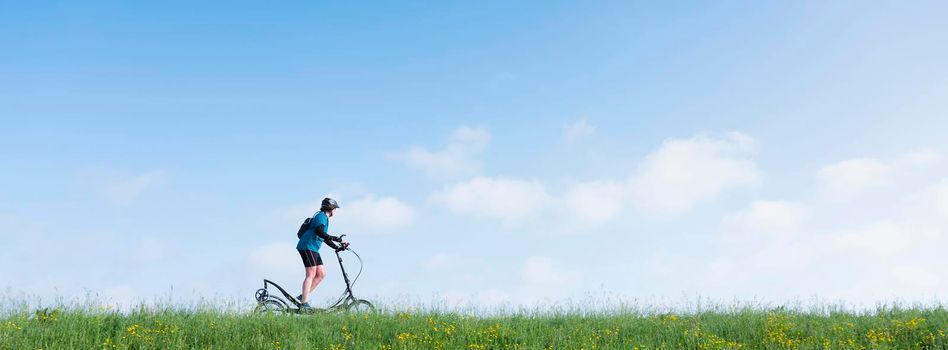 nijkerk, netherlands, 13 may 2021: woman rides elliptigo bike on grassy dike in holland under blue sky in spring