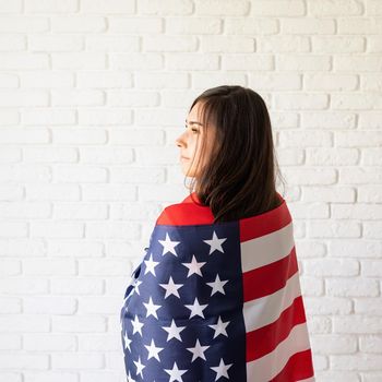 Independence day of the USA. Happy July 4th. Young smiling woman with national flag of the USA, rear view