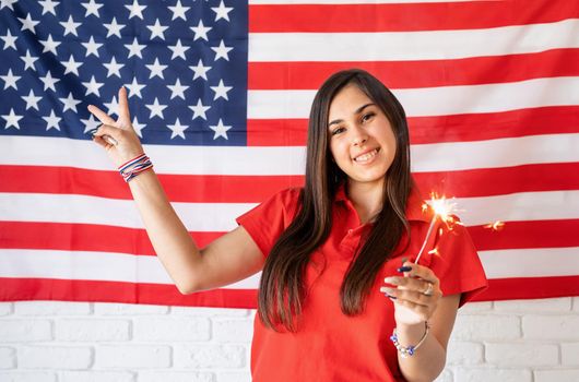 Independence day of the USA. Happy July 4th. Sparkling Bengal fire in caucasian woman hand. Beautiful woman holding a sparkler on US flag background