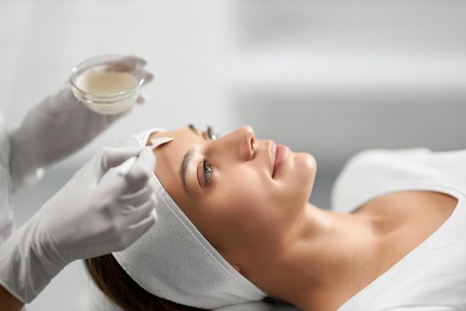 Side view of beautician in white rubber gloves holding moisturizing cream and applies to the patient's face. Concept of special beauty procedure for improvements skin with different mask for face. 