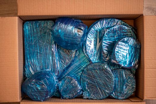 Glassware wrapped with blue wrapping nylon at the bottom of a cardboard box. High quality photo