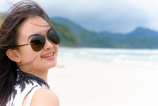 Close-up face beautiful woman tourist wearing sunglasse looking at the camera and smiling with happy on the beach and sea in summer at Tarutao island, Satun, Thailand