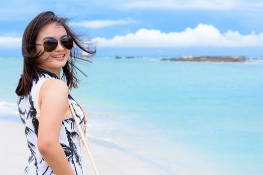 Beautiful woman tourist wearing sunglasse looking at the camera and smiling with happy on the beach and sea in summer sky background at Koh Tarutao island, Satun, Thailand