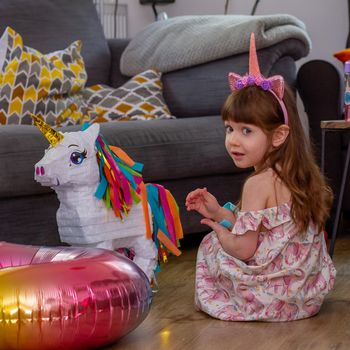 A Cute Baby Girl Sitting On The Floor With a Balloon And An Unicorn Pinata